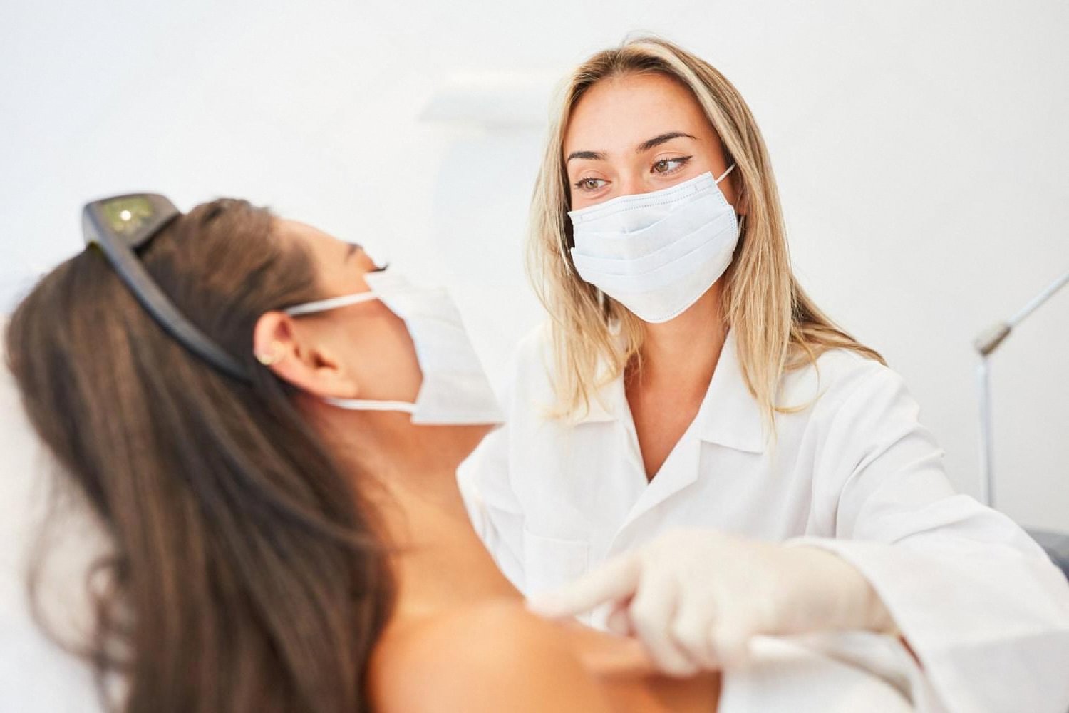 Aesthetic practitioner in mask and gloves preparing a client for a laser facial procedure