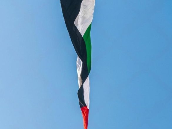 UAE national flag flying above a white monument against a clear blue sky