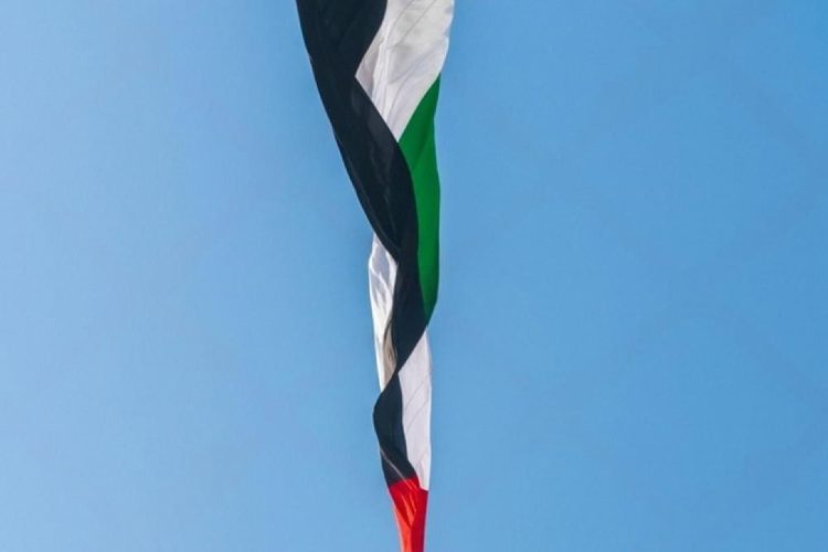UAE national flag flying above a white monument against a clear blue sky